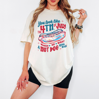 Woman wearing a cream oversized t-shirt with a red, white, and blue hot dog graphic and patriotic text that says "You Look Like the 4th of July – Makes Me Want a Hot Dog Real Bad," styled with black biker shorts.