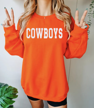 Person wearing an orange sweatshirt with 'COWBOYS' text, making peace signs.