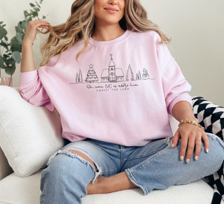 Person wearing a pink sweatshirt with a graphic design and text, sitting on a couch.