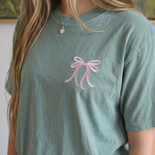 Green t-shirt with a pink bow design worn by a person.