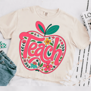 Boho teacher shirt with pink and floral apple graphic and the word Teach, modeled with casual summer outfit