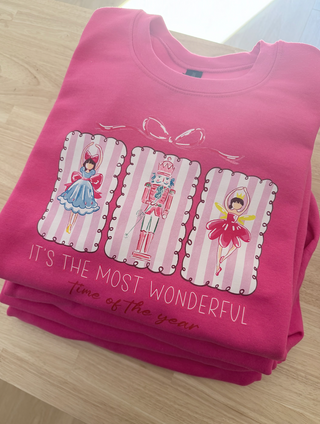 Stack of pink shirts with festive designs and text on a light wooden surface