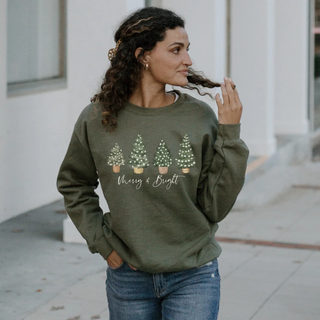 Woman wearing a green sweatshirt with Christmas tree design and text, standing on a sidewalk.